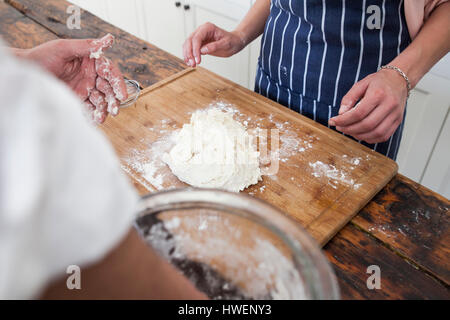 Over shoulder view of hands of two women preparing dough on chopping board Stock Photo