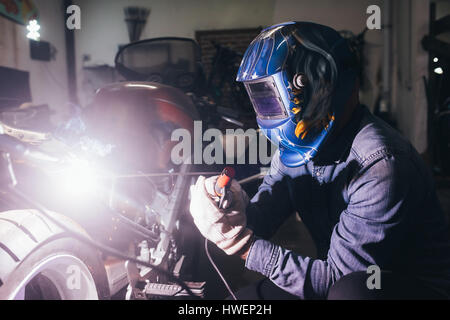 Mature man in garage, working on motorcycle, using welding equipment Stock Photo