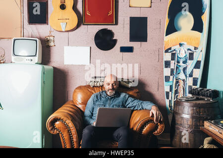 Mature man sitting in armchair, using laptop Stock Photo