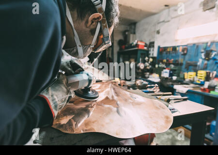 Metalworker polishing copper in forge workshop Stock Photo