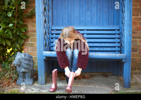 Girl putting on boots on arbour bench Stock Photo