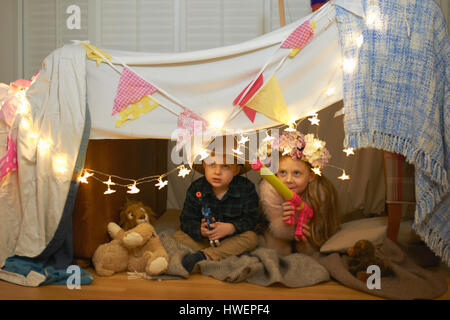 Girl and brother hiding in den with toy guns Stock Photo