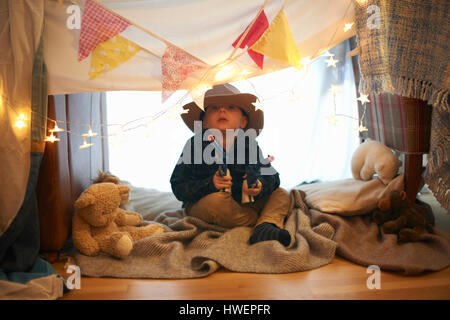 Portrait of cute boy in cowboy hat holding toy guns in bedroom den Stock Photo