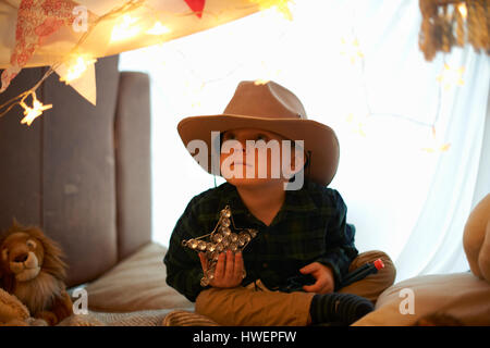 Portrait of cute boy in cowboy hat holding star in bedroom den Stock Photo