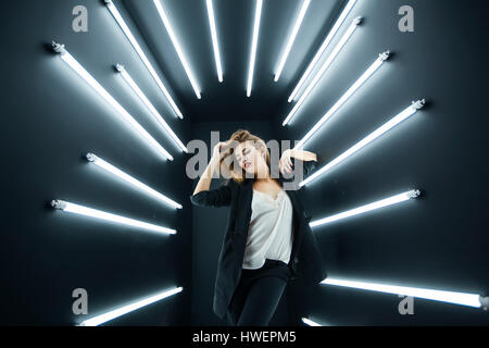 Young fashion model posing in studio, electric lighting behind her Stock Photo