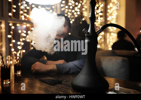 man holding hookah pipe and smoking in a night club  Stock Photo