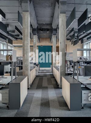 Hall in a loft style in the office with concrete columns and a gray carpet on the floor. There are workplaces with computers and shelves and lockers,  Stock Photo