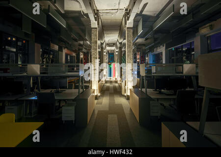 Luminous office in a loft style with gray walls, concrete columns and a carpet. There are many workplaces with computers and metal reticulated shelves Stock Photo