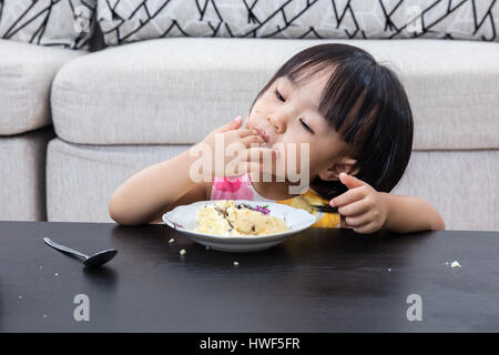 Asian Chinese little girl eating birthday cheese cake at home indoor. Stock Photo