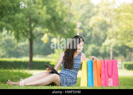beautiful asian woman using digital tablet shopping online choose sitting on grass. outdoors background. technology and people concept Stock Photo