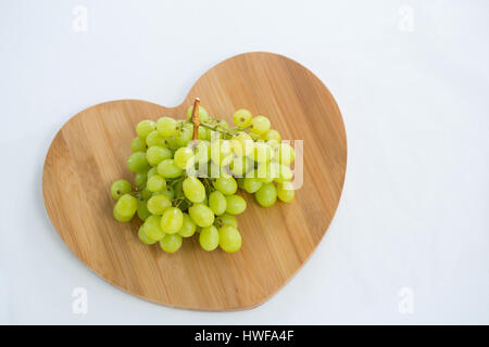 Overhead of green bunch of grapes on chopping board against white background Stock Photo