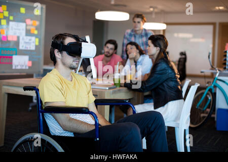 Physically disabled man on wheelchair using VR headset in office Stock Photo
