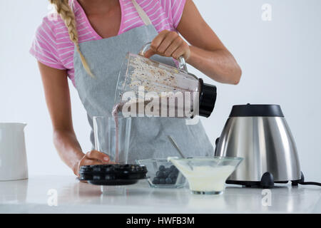 Woman pouring smoothie into glass at counter in kitchen Stock Photo