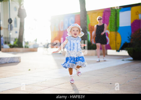A little girl in a blue dress and Panama joyfully runs Stock Photo