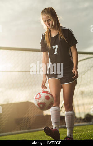 Low angle view of soccer player kicking ball on field under sunset sky Stock Photo