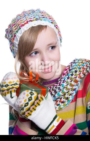Smiling pretty young girl wearing coloful knitted scarf, hat and mittens, holding christmas gift isolated on white background. Winter clothes and chri Stock Photo
