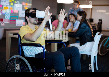 Physically disabled man on wheelchair using VR headset in office Stock Photo