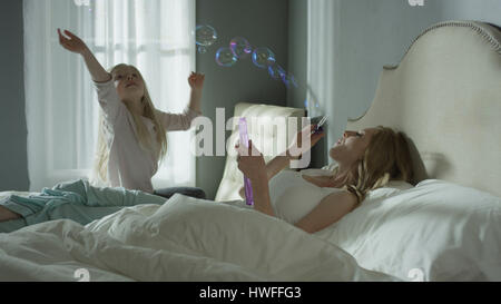Mother and daughter playing and blowing bubbles in bedroom Stock Photo