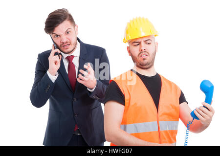 Angry entrepreneur talking on mobile phone near young constructor isolated on white background Stock Photo