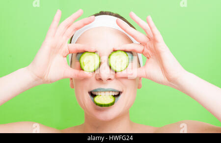 Attractive girl with slices of cucumber on eyes  smiling happy isolated on green background in closeup view Stock Photo