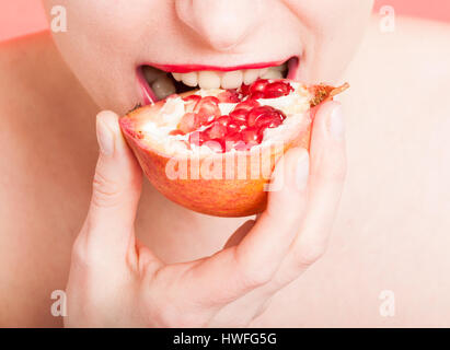 Woman mouth in closeup eating fresh pomegranate. Healthy food concept isolated on red background Stock Photo