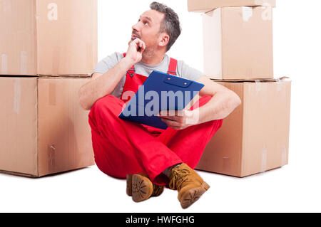 Mover guy sitting on the floor holding clipboard  surrounded by boxes and checking something or counting isolated on white background Stock Photo