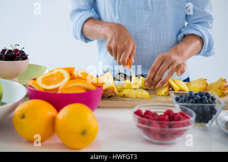 Mid-section of woman cutting fruits on chopping board against white background Stock Photo
