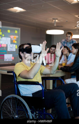 Physically disabled man on wheelchair using VR headset in office Stock Photo