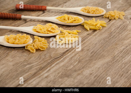 Spoons filled with varieties of pasta on wooden background Stock Photo