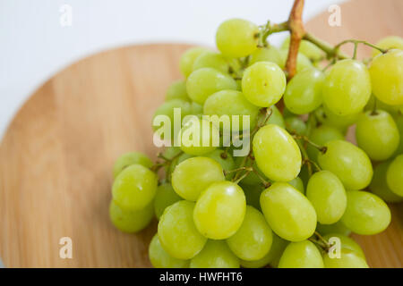 Close-up of green bunch of grapes on chopping board against white background Stock Photo