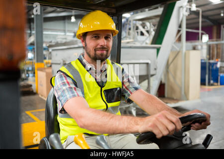 Portrait of young male worker driving forklift in warehouse Stock Photo