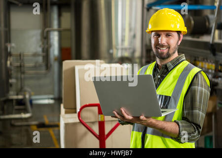 Portrait of smiling male worker using laptop in distribution warehouse Stock Photo