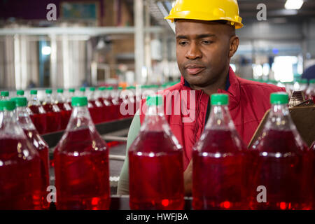 Serious male worker monitoring red juice bottles in factory Stock Photo