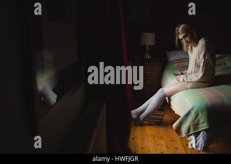Woman sitting and using mobile phone on bed in bedroom Stock Photo