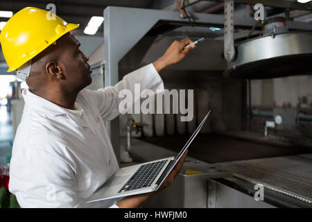 Male worker wearing lab coat while using laptop in juice factory Stock Photo