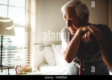 Thoughtful senior man with his walking stick in the bedroom at home Stock Photo