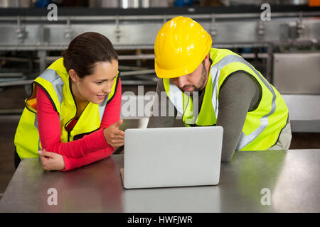 Male and female workers using laptop in factory Stock Photo