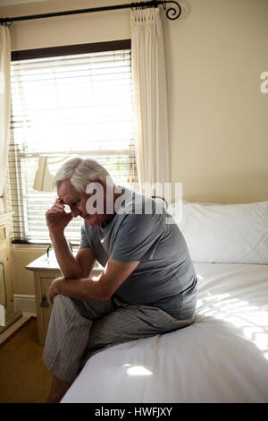 Worried senior man sitting on bed in the bedroom at home Stock Photo