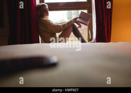 Woman sitting on window and reading a book at home Stock Photo