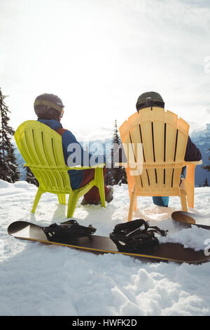 Rear view of couple sitting on mountain against sky during winter