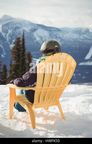 Rear view of woman sitting on chair at snow covered mountain against sky