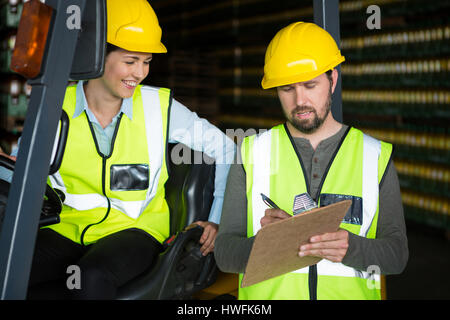Smiling female worker looking at male worker writing on clipboard at warehouse Stock Photo