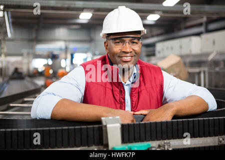 Portrait of smiling male employee standing by conveyor belt in factory Stock Photo