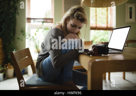 Thoughtful woman sitting with laptop at home Stock Photo