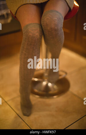 Woman sitting on a stool in kitchen at home Stock Photo