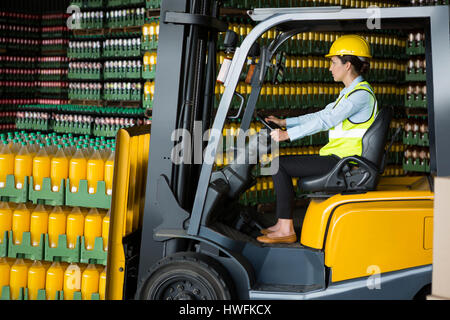 Side view of confident female worker driving forklift in warehouse Stock Photo