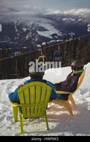 Couple sitting on chair at mountain during winter