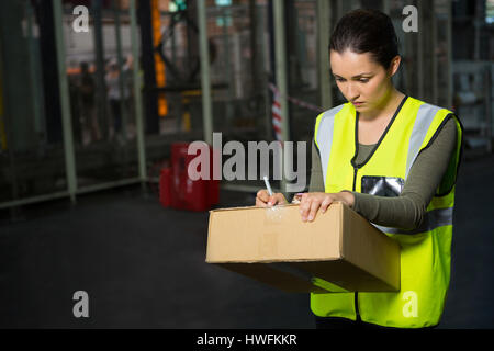 Confident female worker writing on box in warehouse Stock Photo