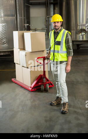 Full length portrait of male worker pulling trolley in warehouse Stock Photo