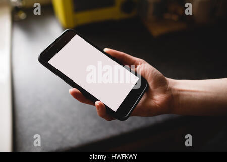 Womans hand holding mobile phone in the kitchen at home Stock Photo